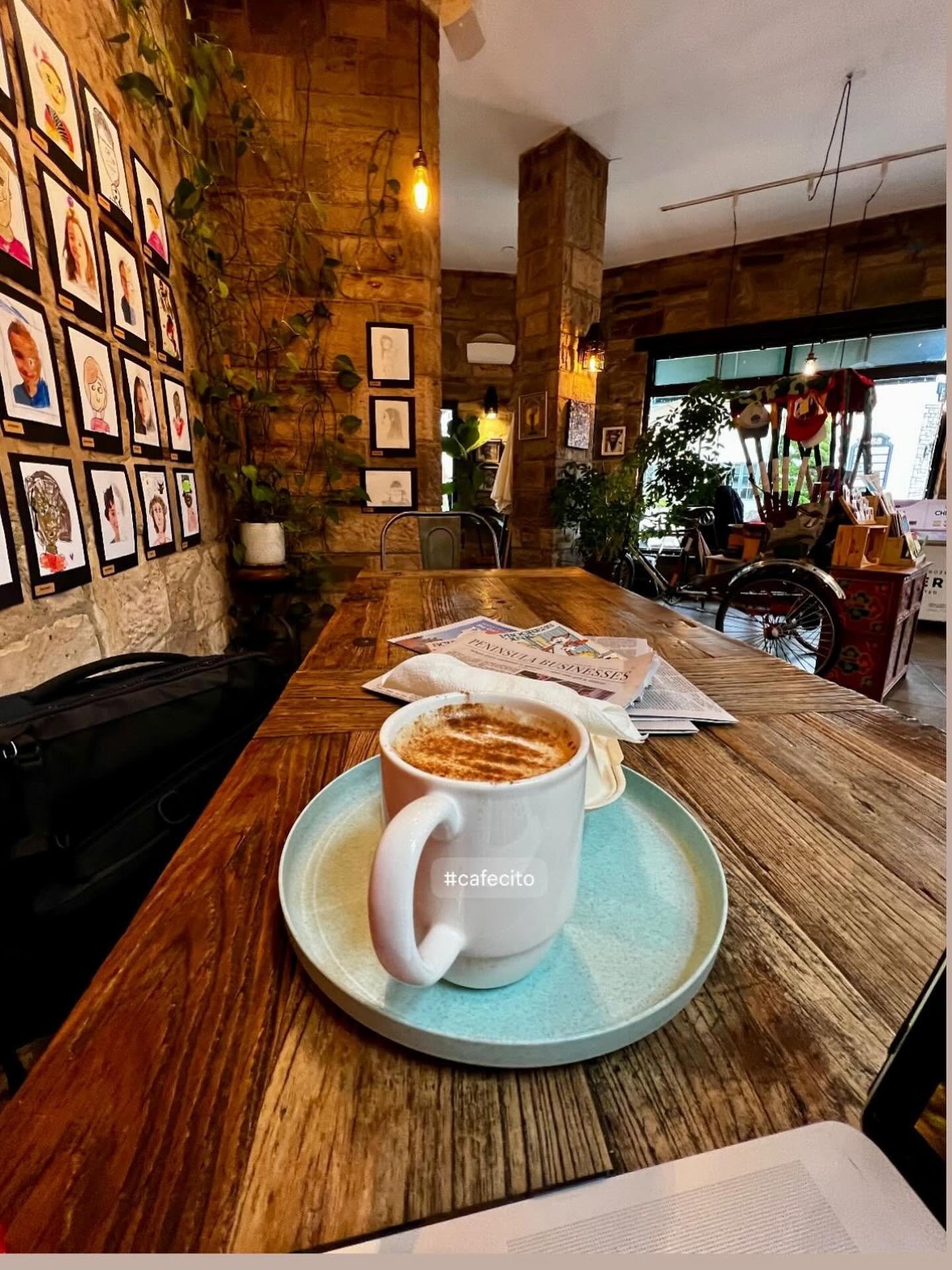 A cafecito on a reclaimed-wood table inside East Village Cafe, ivy and art on the Carmel-stone walls
